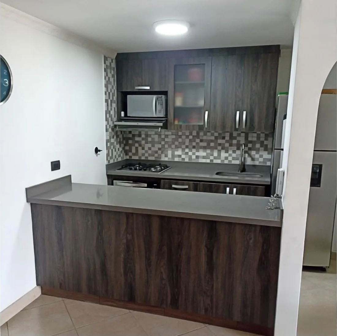 Cocina construida en laminado carbono con barra hacia la sala, mesón gris, nicho para microondas y salpicadero en mosaico