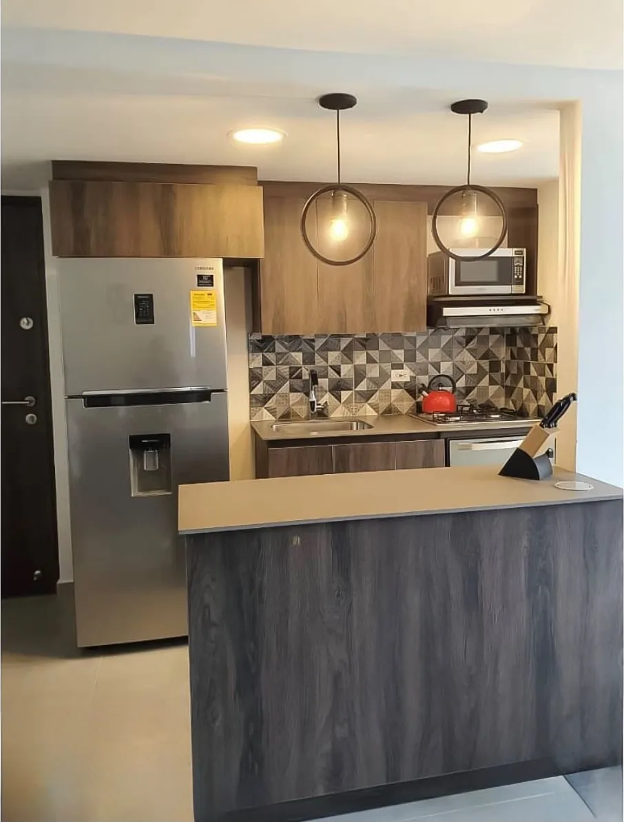 Cocina construida en laminado macadamia oscuro con barra de desayuno, lámparas colgantes y salpicadero en mosaico geométrico