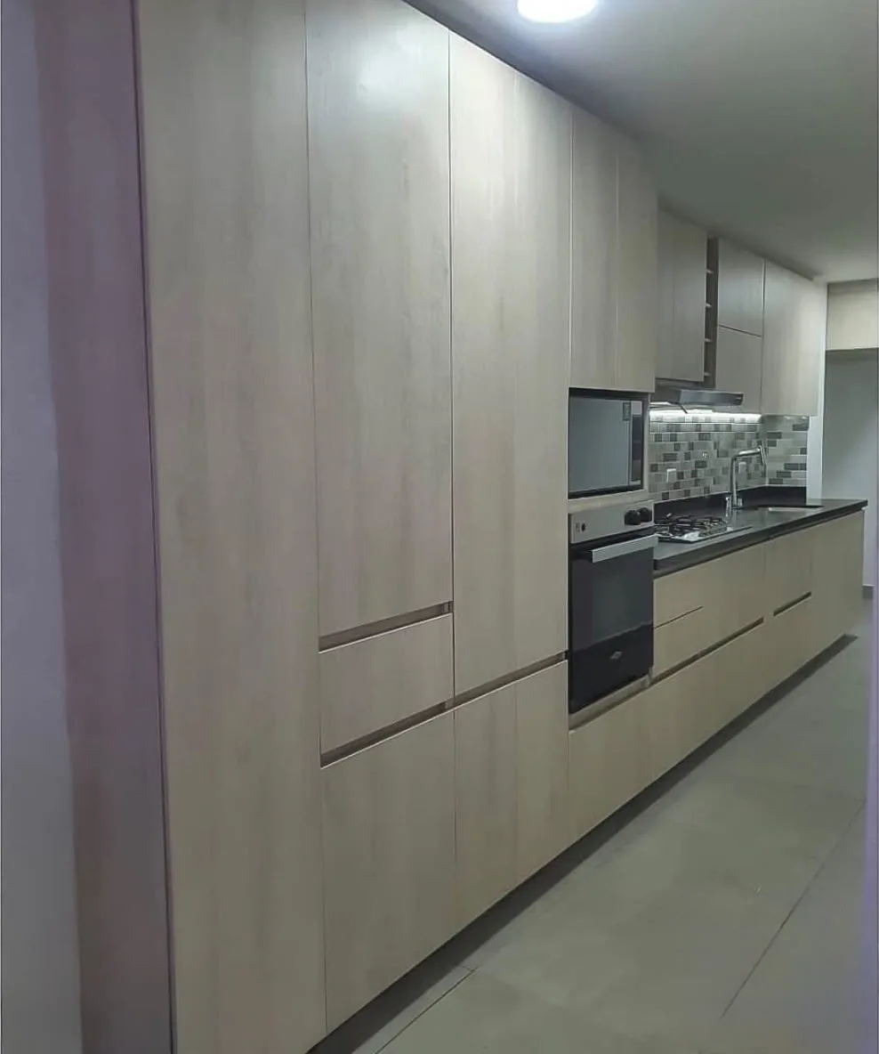 Cocina lineal construida en laminado Artiko con torre de despensa, horno empotrado y mesón gris oscuro